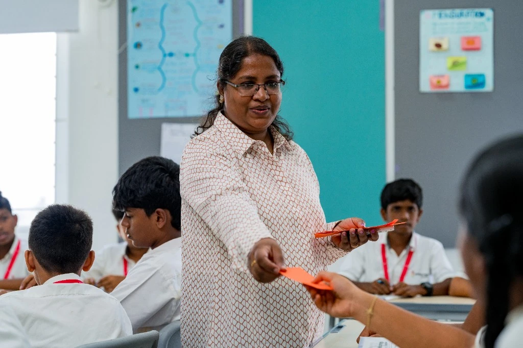 A Wellsprings teacher handing cards to students in class.