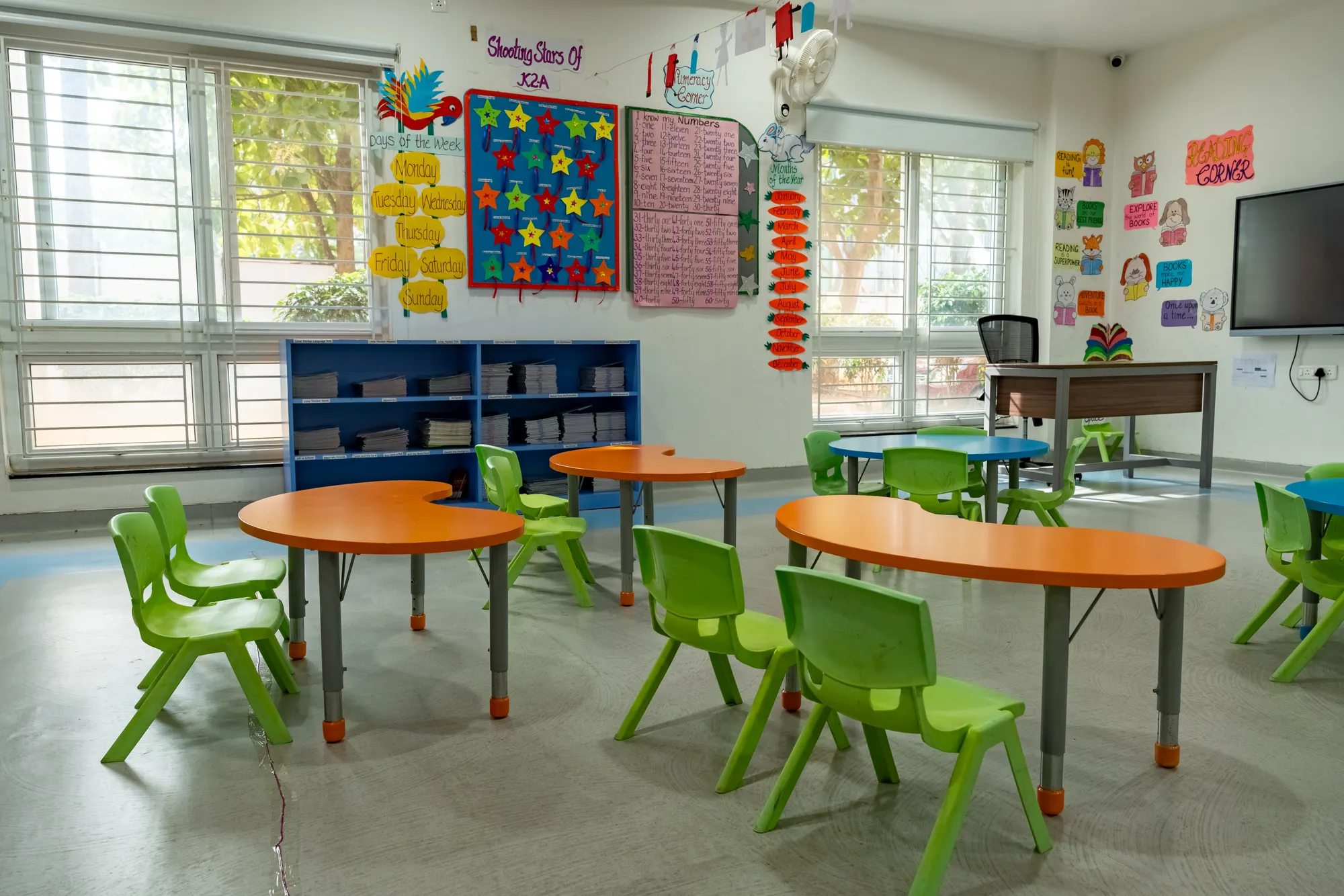 A bright classroom with small tables and green chairs