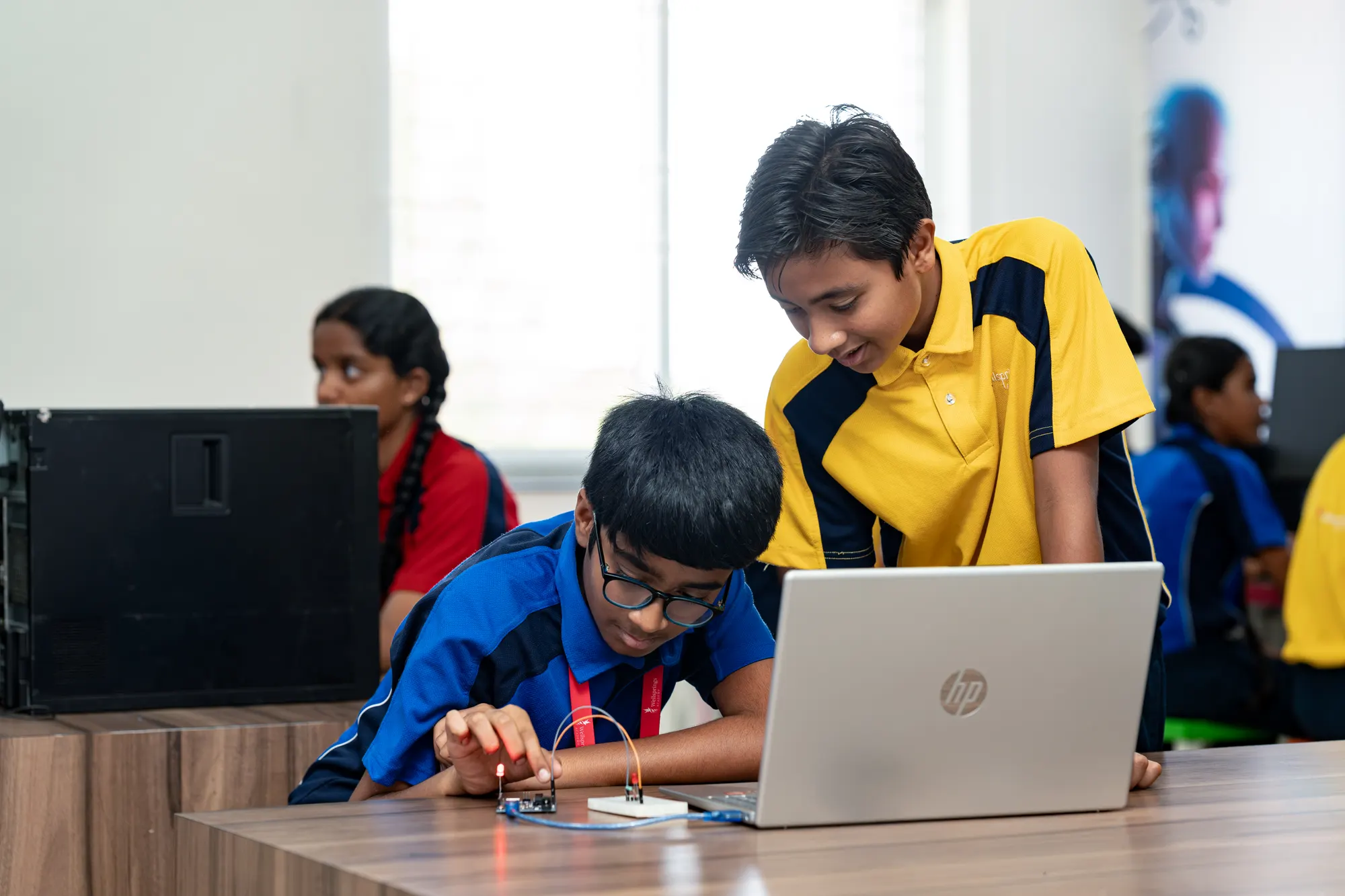 Two Wellsprings students building a small circuit beside a laptop